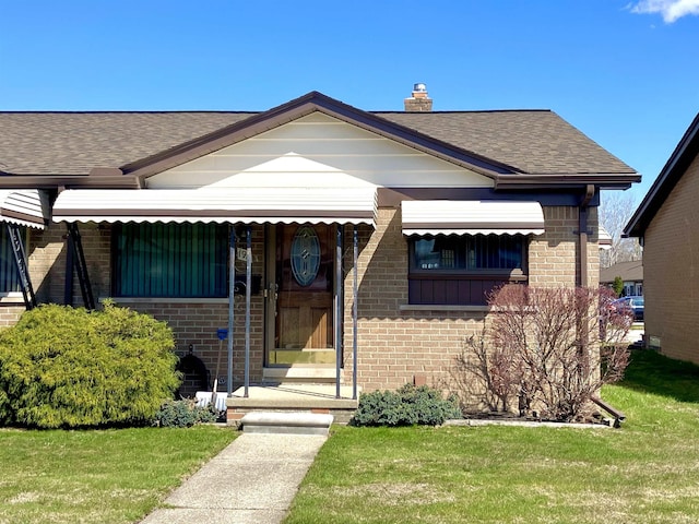 bungalow-style house featuring brick siding, a shingled roof, a chimney, and a front lawn