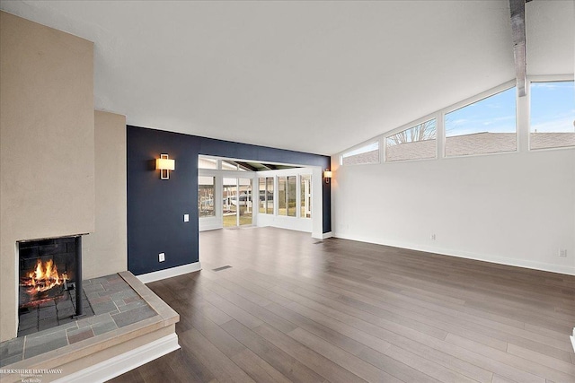 unfurnished living room featuring baseboards, a wealth of natural light, a lit fireplace, and lofted ceiling with beams
