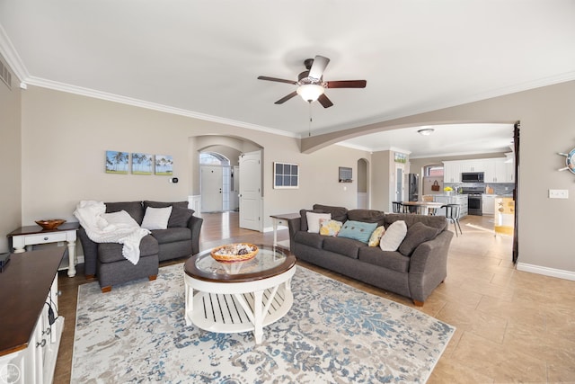 living room featuring arched walkways, baseboards, ceiling fan, crown molding, and light tile patterned floors