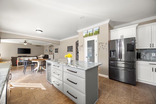 kitchen featuring a ceiling fan, decorative backsplash, stainless steel fridge, arched walkways, and ornamental molding