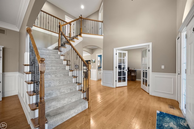interior space with light wood-type flooring, french doors, a high ceiling, and arched walkways