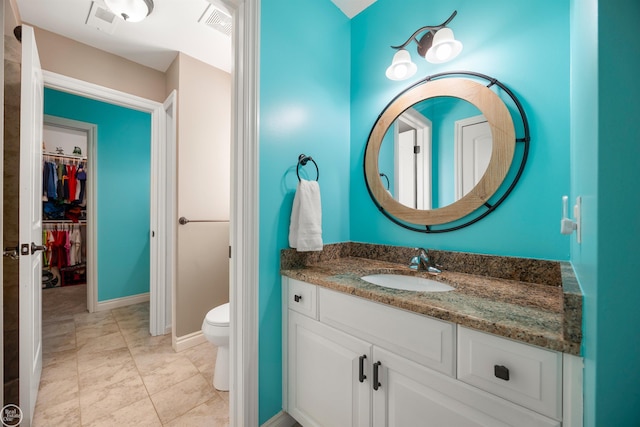 bathroom featuring visible vents, vanity, a walk in closet, and toilet