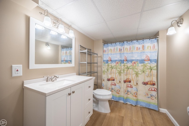 bathroom with wood finished floors, toilet, vanity, a shower with shower curtain, and a paneled ceiling