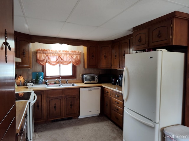 kitchen featuring a paneled ceiling, a sink, white appliances, and light countertops