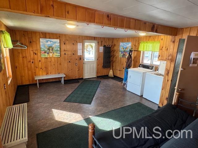clothes washing area featuring a wealth of natural light, independent washer and dryer, dark floors, wooden walls, and laundry area