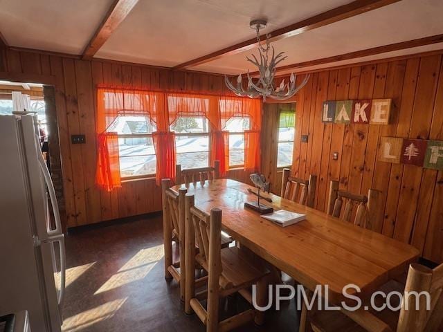 dining room featuring beamed ceiling, wood walls, and a notable chandelier