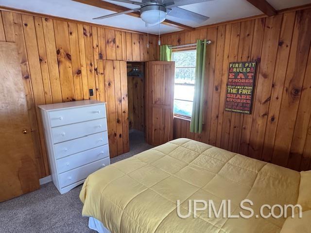 carpeted bedroom featuring beam ceiling and wood walls