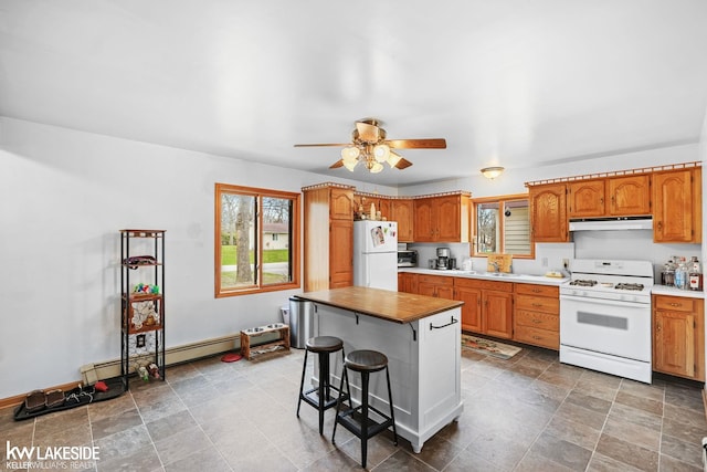 kitchen with under cabinet range hood, white appliances, a sink, and brown cabinets