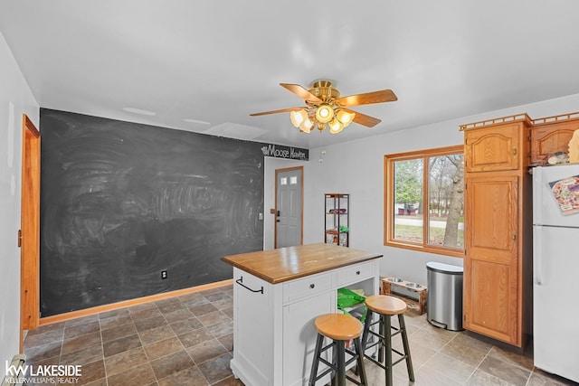 kitchen featuring wood counters, freestanding refrigerator, a kitchen island, and ceiling fan