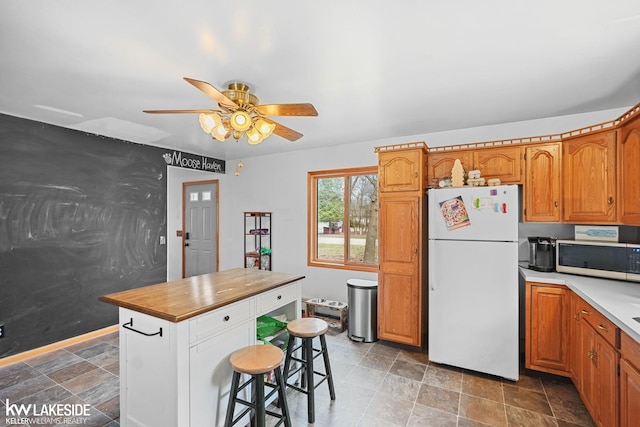 kitchen with brown cabinets, a ceiling fan, freestanding refrigerator, and stainless steel microwave