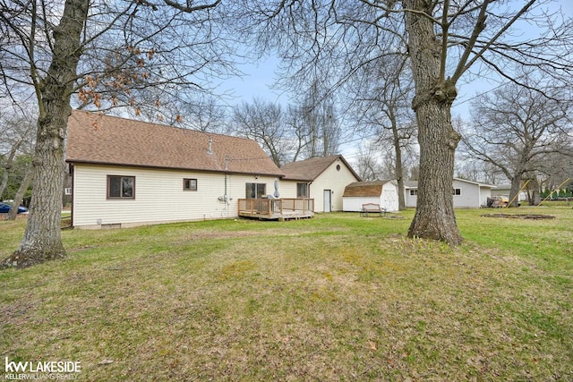 rear view of house with a storage shed, a yard, an outdoor structure, roof with shingles, and a deck