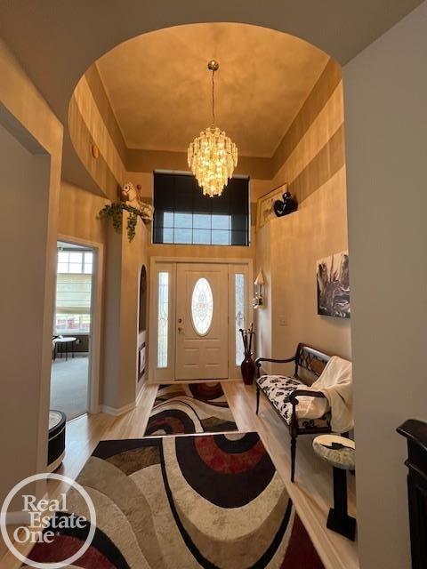 foyer entrance with wood finished floors, arched walkways, and a chandelier