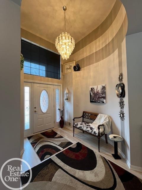 foyer with baseboards, wood finished floors, a towering ceiling, and an inviting chandelier