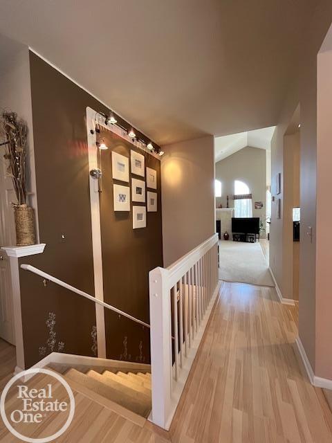 corridor with lofted ceiling, baseboards, light wood finished floors, and an upstairs landing