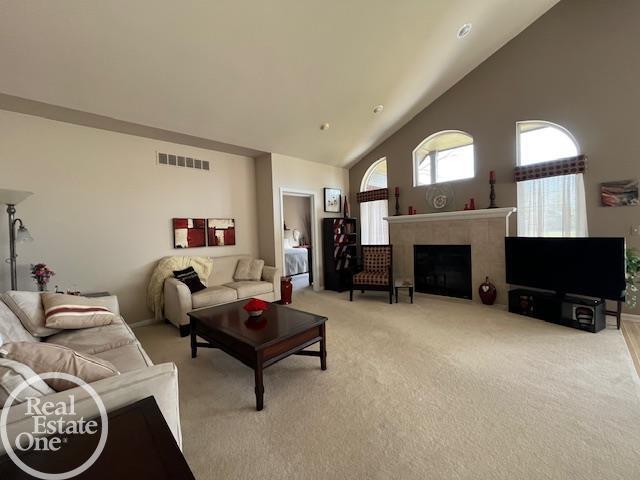 living area with light carpet, a fireplace, visible vents, and high vaulted ceiling
