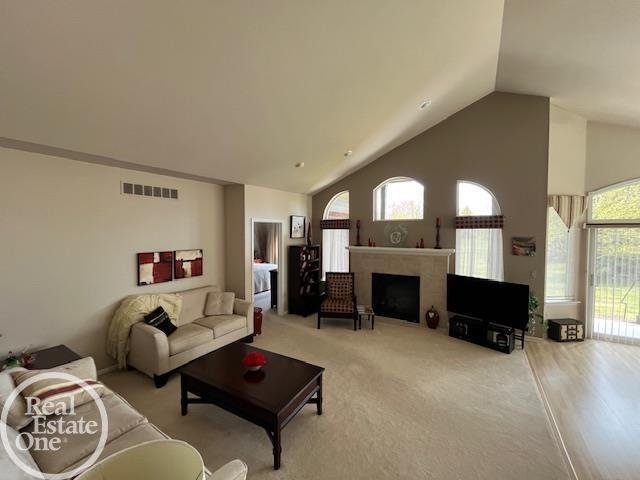 living room featuring light colored carpet, high vaulted ceiling, visible vents, and a fireplace