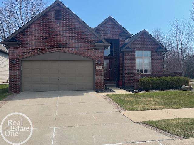 view of front of house with brick siding, an attached garage, driveway, and a front lawn