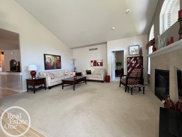 living room with visible vents, light carpet, baseboards, a glass covered fireplace, and high vaulted ceiling