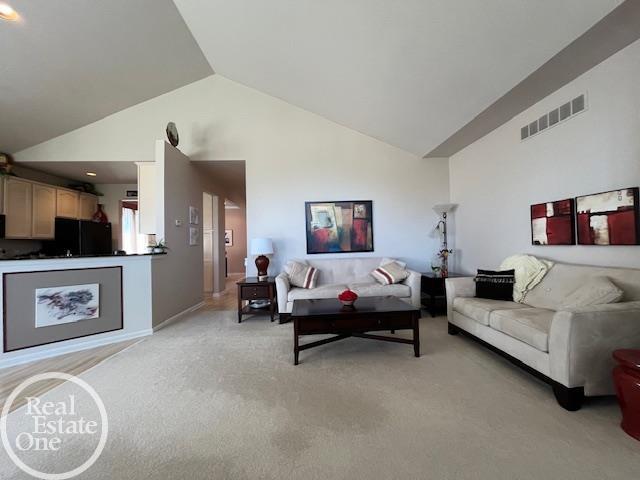 living room with baseboards, visible vents, high vaulted ceiling, and light carpet