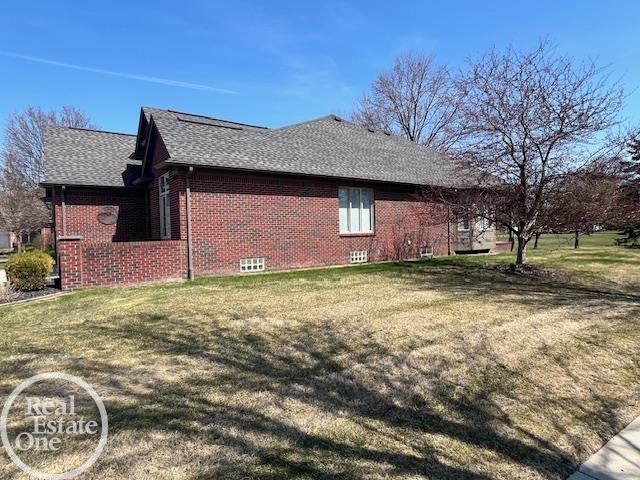 view of side of property featuring a yard, brick siding, and roof with shingles