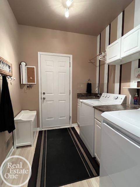 laundry area with separate washer and dryer, light wood-style flooring, baseboards, and cabinet space