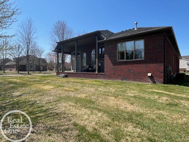 rear view of property with a lawn, covered porch, and brick siding