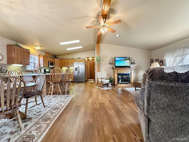 living room featuring lofted ceiling, a ceiling fan, a glass covered fireplace, and light wood-style flooring