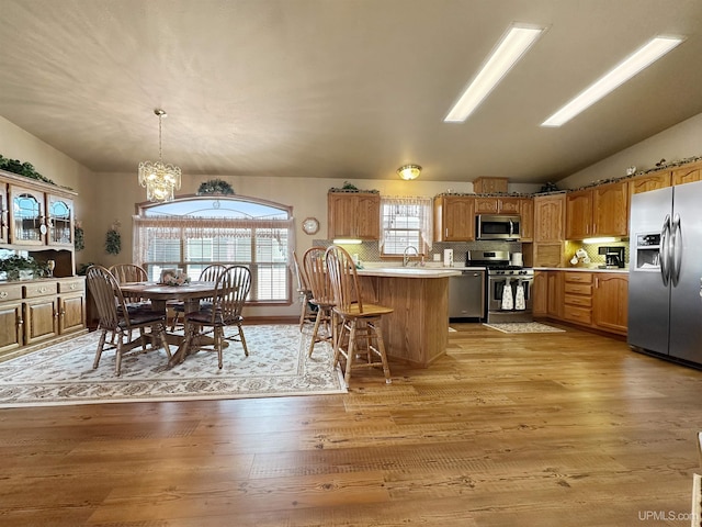 kitchen with a sink, light wood-type flooring, appliances with stainless steel finishes, a peninsula, and a notable chandelier