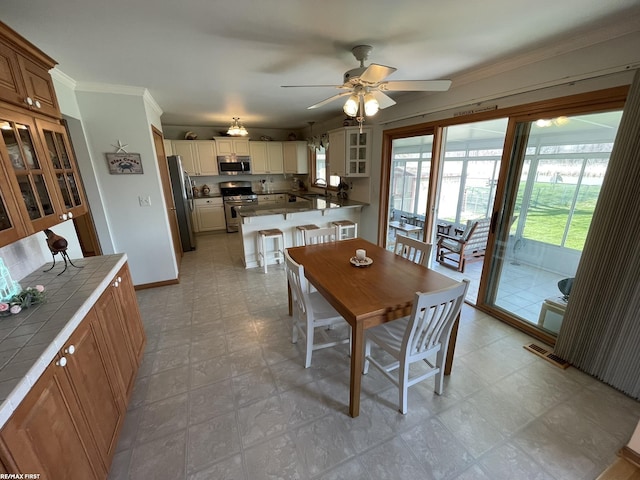 dining area featuring light floors, ceiling fan, baseboards, ornamental molding, and visible vents