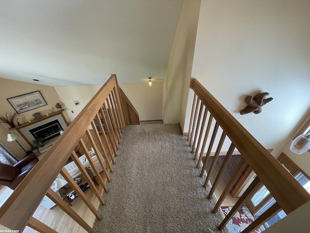 stairway with a glass covered fireplace and carpet flooring