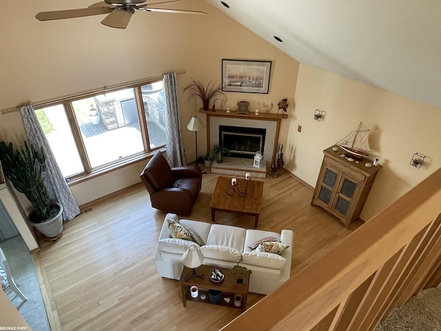 living area featuring light wood-style flooring, a tile fireplace, vaulted ceiling, and ceiling fan