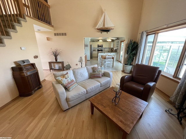 living area with baseboards, light wood-style flooring, visible vents, and a high ceiling