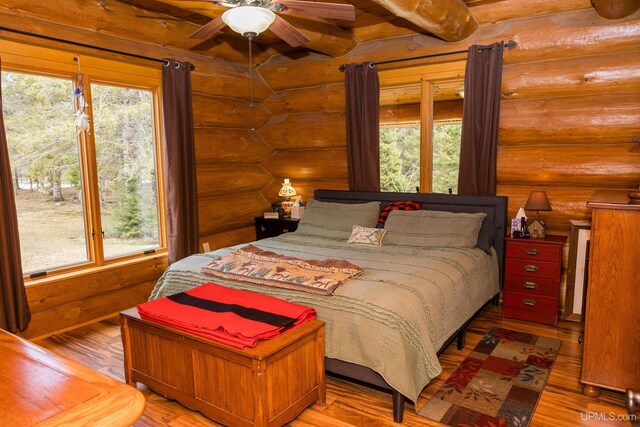 bedroom featuring log walls, wood finished floors, and multiple windows
