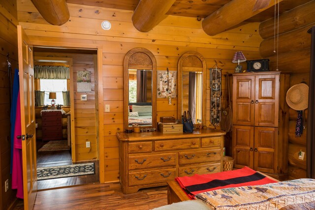 bedroom featuring beamed ceiling, wooden walls, and wood finished floors