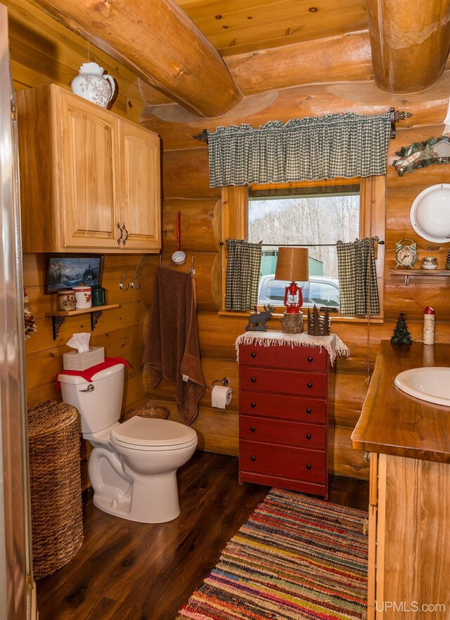 half bath featuring wood finished floors, log walls, vanity, and toilet