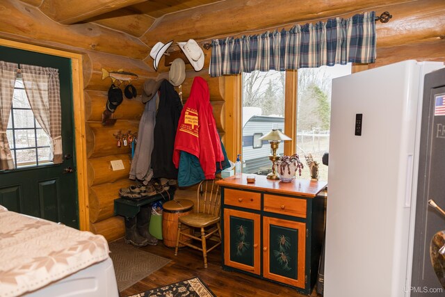 bedroom featuring wood finished floors, freestanding refrigerator, and rustic walls