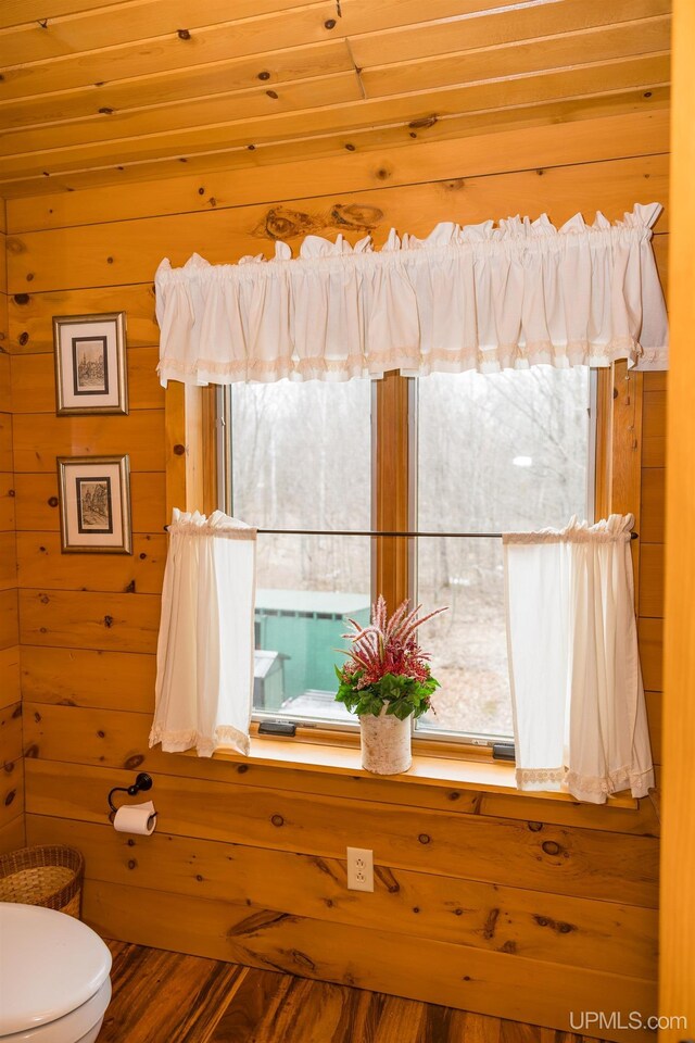 bathroom featuring toilet, wood finished floors, wood walls, and a healthy amount of sunlight