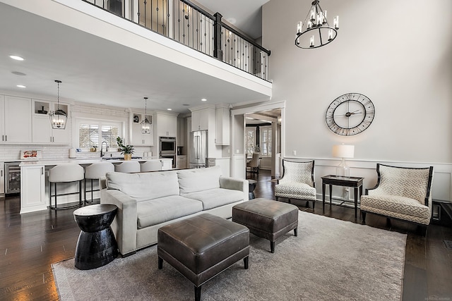 living area with wainscoting, wine cooler, an inviting chandelier, and dark wood finished floors
