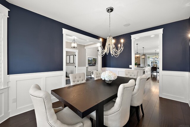 dining area with dark wood finished floors, a decorative wall, a wainscoted wall, and a chandelier