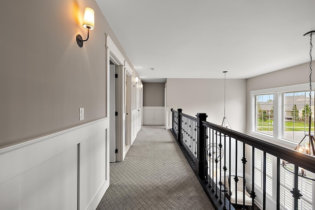 hallway with wainscoting, a decorative wall, an upstairs landing, and carpet
