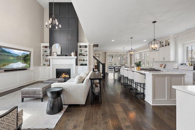 living room with dark wood finished floors, an inviting chandelier, recessed lighting, a warm lit fireplace, and a decorative wall