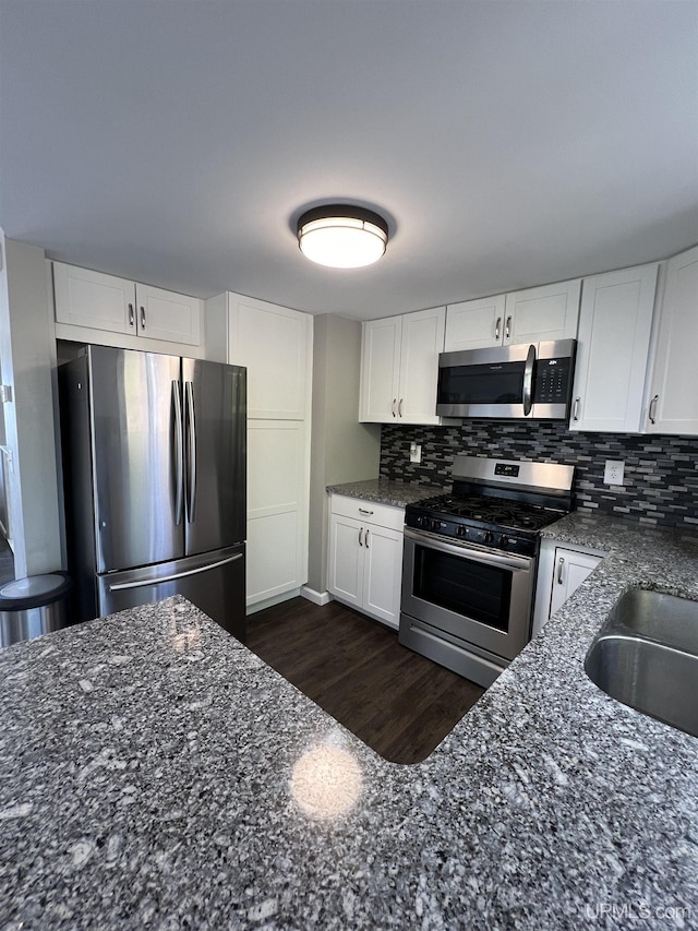 kitchen featuring white cabinets, appliances with stainless steel finishes, dark stone counters, and decorative backsplash