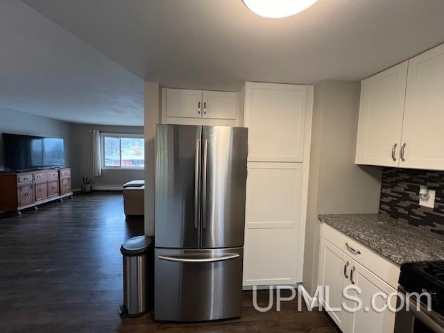 kitchen with freestanding refrigerator, dark wood-style flooring, dark stone counters, decorative backsplash, and white cabinetry
