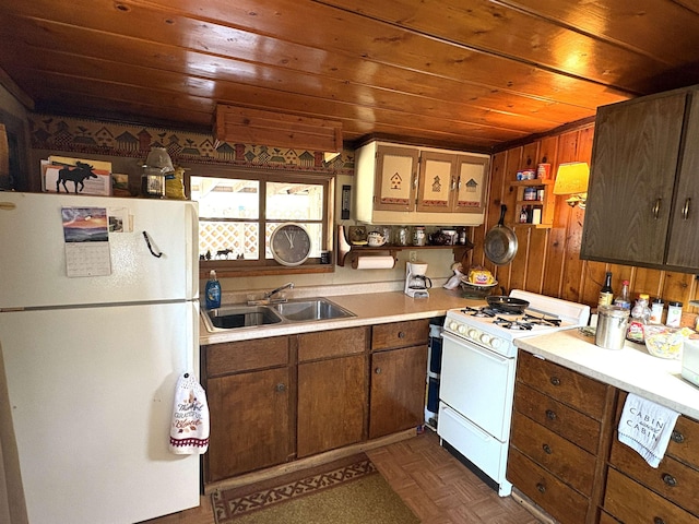 kitchen with white appliances, wood ceiling, light countertops, a sink, and wooden walls