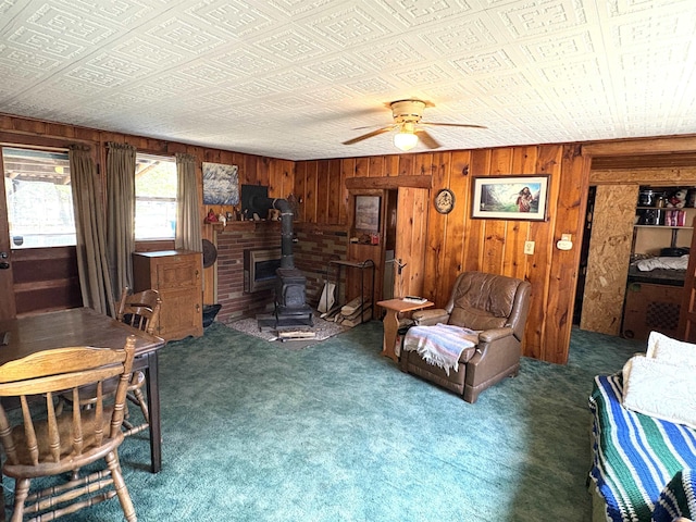 carpeted living room with wood walls, an ornate ceiling, ceiling fan, and a wood stove