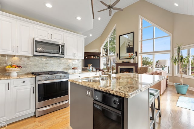 kitchen with white cabinets, high vaulted ceiling, appliances with stainless steel finishes, and light stone counters