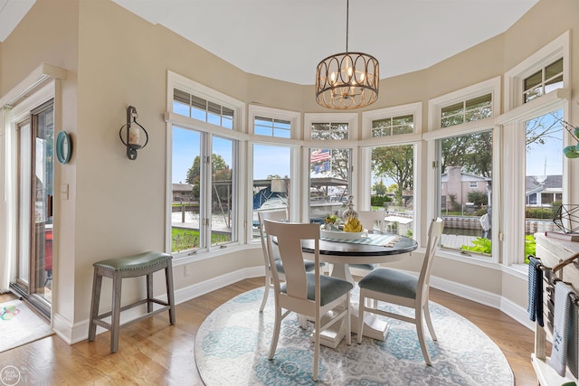 sunroom / solarium with wood finished floors, a chandelier, and baseboards