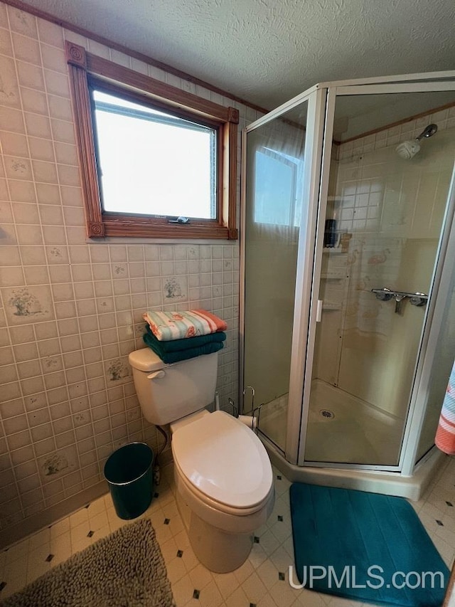 full bath with tile patterned flooring, tile walls, a shower stall, toilet, and a textured ceiling