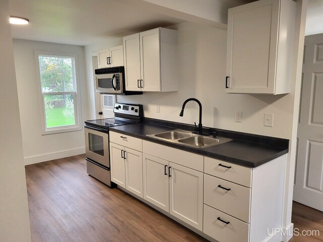 kitchen with white cabinetry, a sink, dark countertops, stainless steel appliances, and wood finished floors