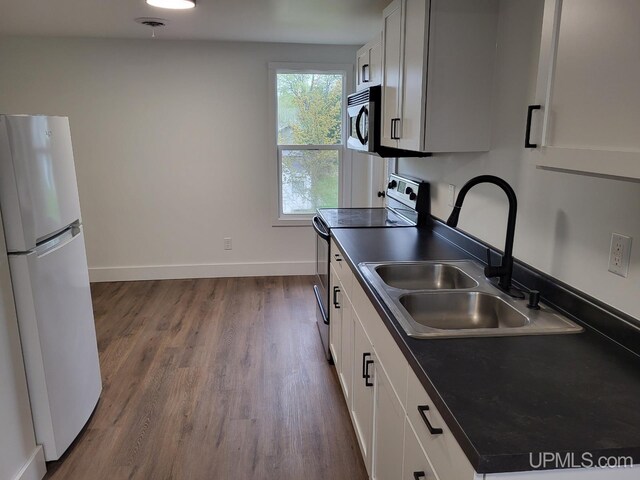 kitchen featuring dark wood-style floors, a sink, stainless steel appliances, baseboards, and dark countertops